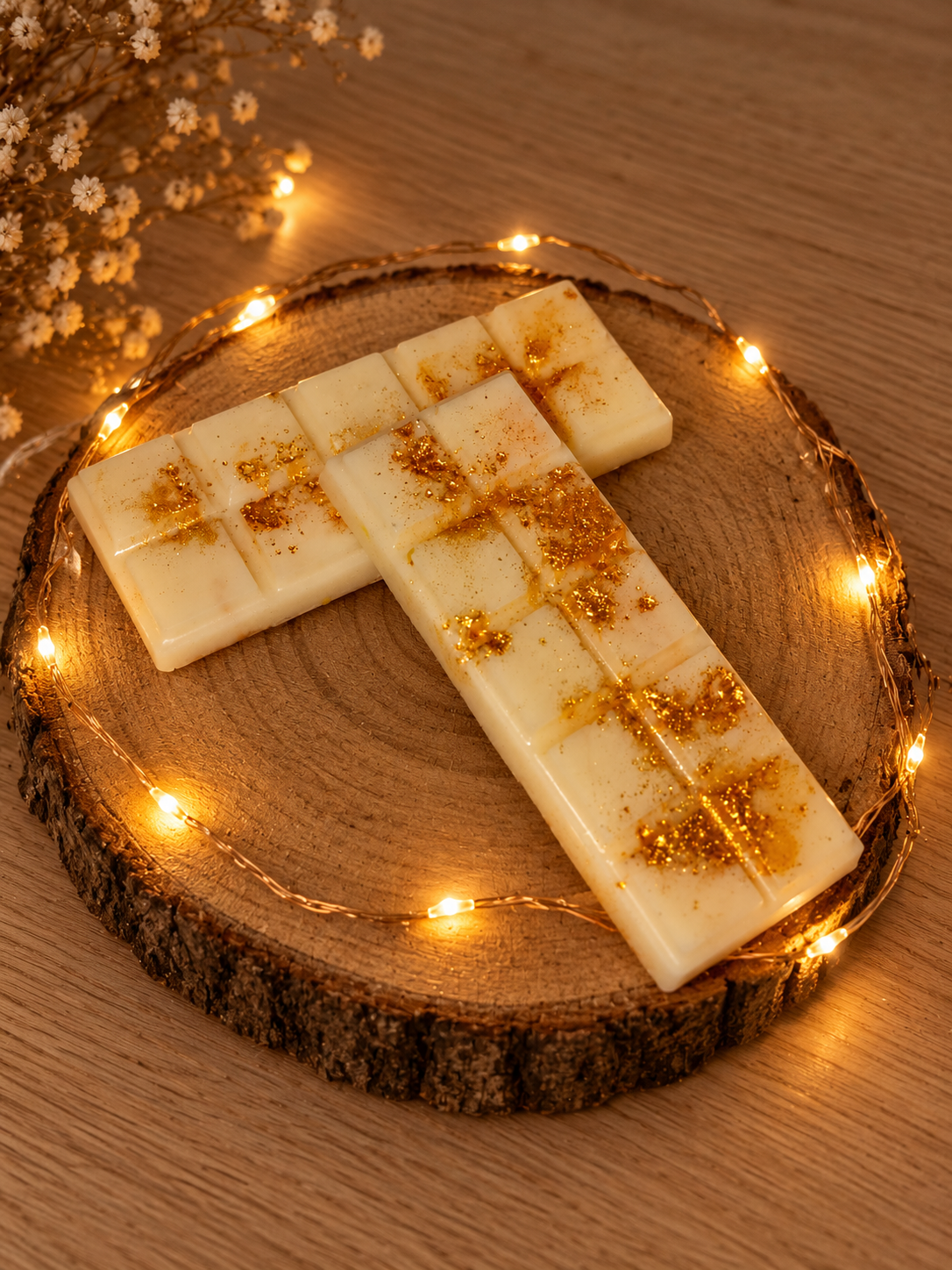 Deux tablettes de fondant parfumé Cannelle Dorée aux éclats dorés, superposées sur un rondin de bois, avec des fleurs séchées en arrière-plan.