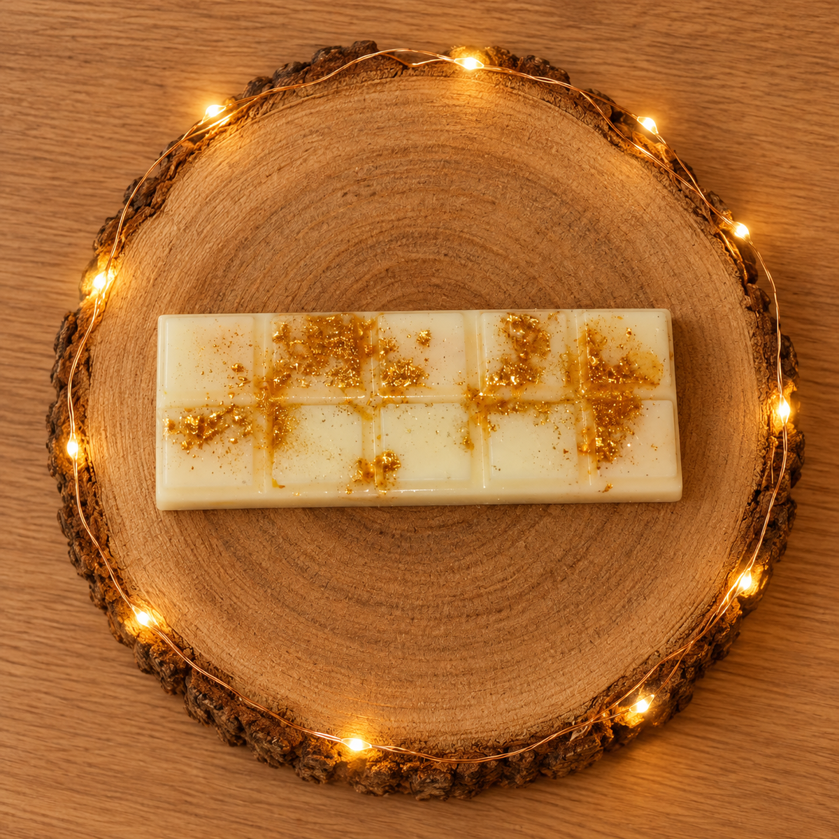 Tablette de fondant parfumé Cannelle Dorée, couleur ivoire et décorée d’éclats dorés, sur un rondin de bois illuminé.