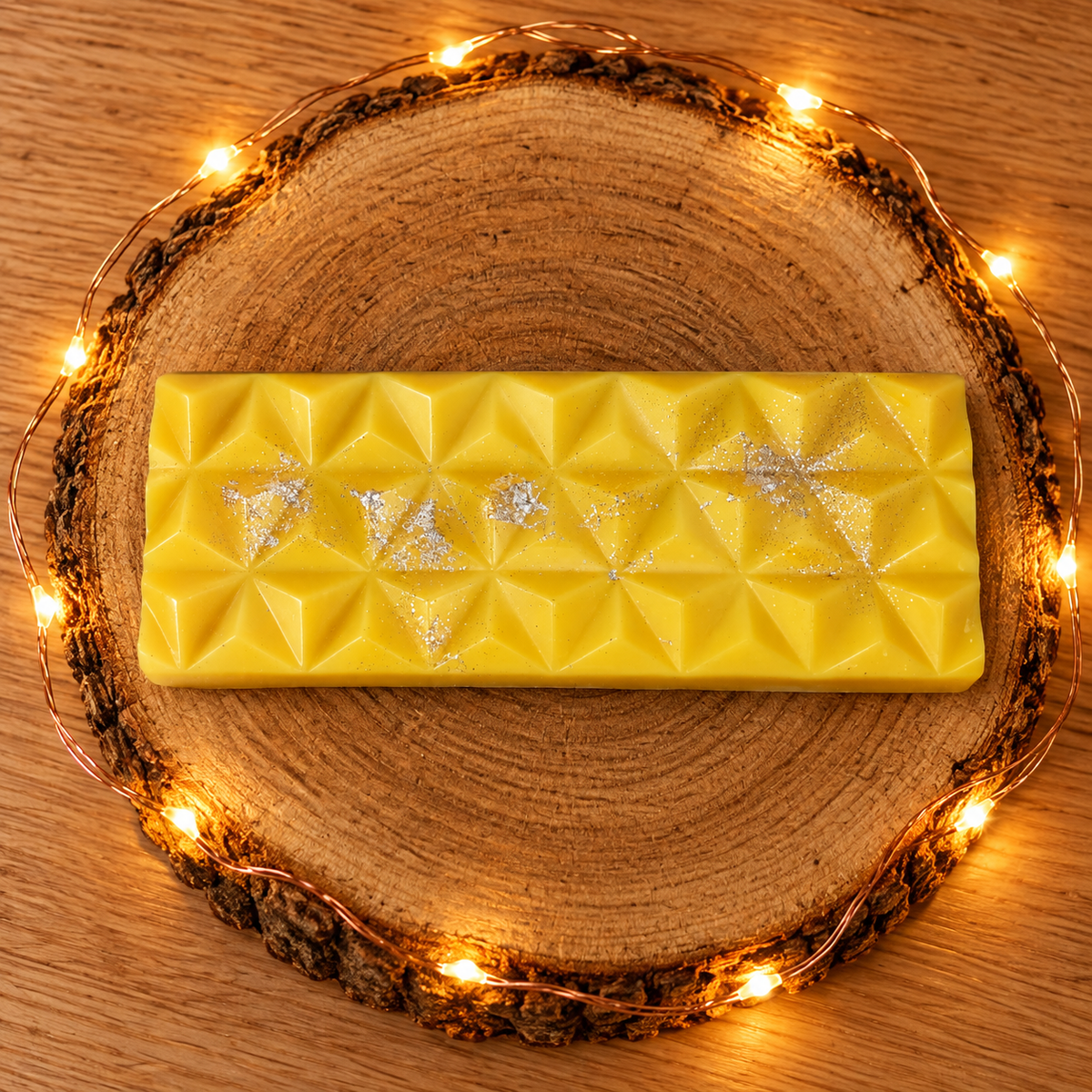 Tablette de fondant parfumé Fleur de Coton jaune, aux motifs géométriques et éclats argentés, sur un rondin de bois illuminé.