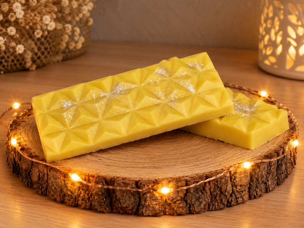Deux tablettes de fondant parfumé Fleur de Coton jaunes, superposées sur un rondin de bois entouré d’une guirlande lumineuse.