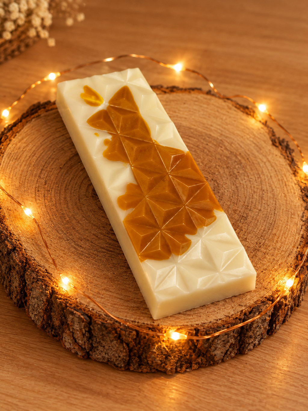 Tablette de fondant Caramel Beurre Salé blanche et couleur caramel, à motifs géométriques, sur un rondin avec une guirlande lumineuse.