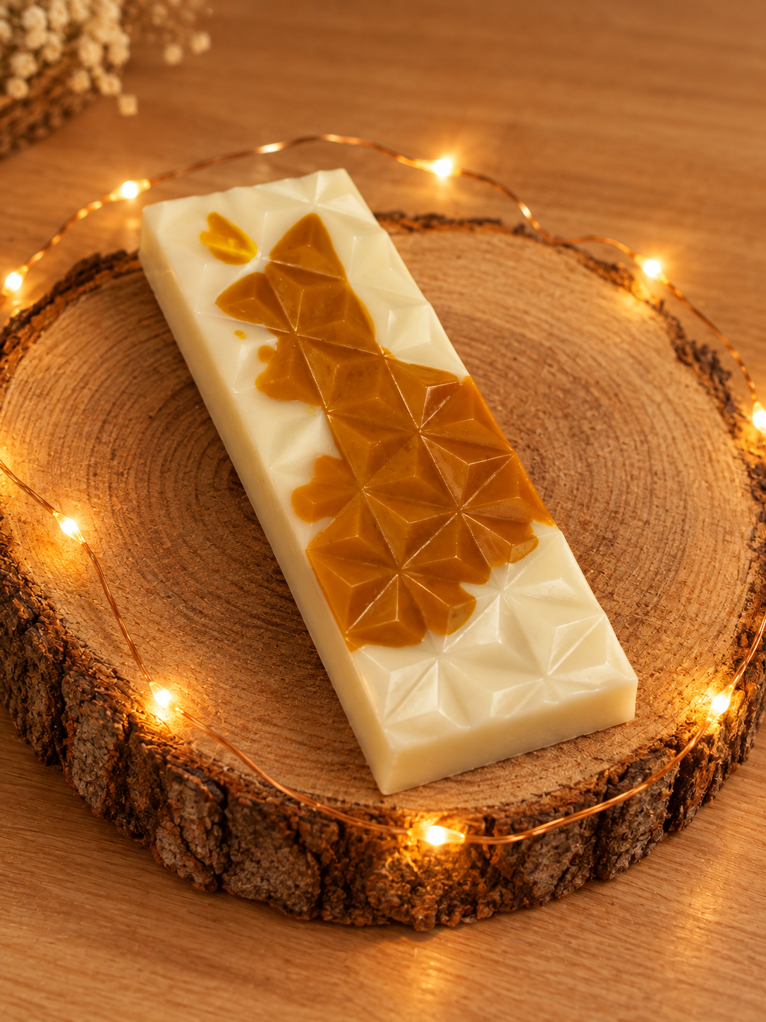 Tablette de fondant Caramel Beurre Salé blanche et couleur caramel, à motifs géométriques, sur un rondin avec une guirlande lumineuse.
