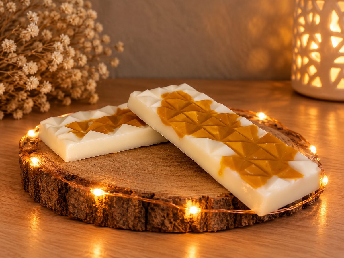Deux tablettes de fondant Caramel Beurre Salé blanches et couleur caramel, vues de trois quarts sur un rondin, devant un photophore.