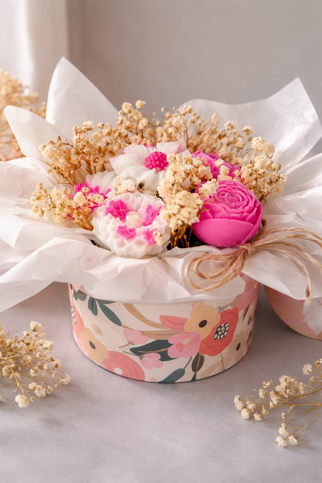 « Box florale ronde avec bougies en cire rose – roses et renoncules, gypsophile séchée, papier de soie blanc et nœud en raphia »